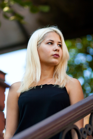 Young beautiful blonde girl posing on the background of the urban landscape. Sexy lady in a black dress with a pleasant appearance.の写真素材