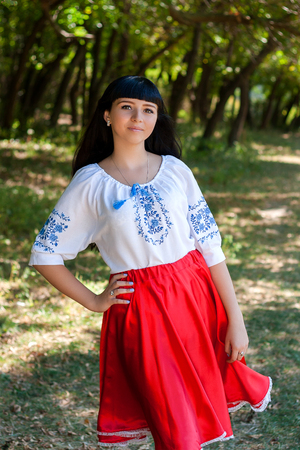 Beautiful young Ukrainian girl in national costume. Girl with beautiful appearance in the woods on the nature. Portrait of beautiful dark-haired young girl with beautiful eyes.の写真素材