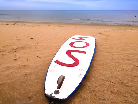 surfboard on the sand  -lanzarote island, spain in a sunny clear day of summer. The surfboard shows in red letters sos that means mayday in the international laguageの写真素材