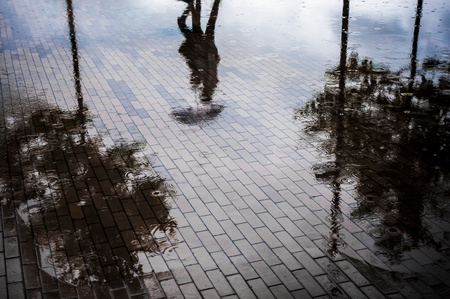Couple with umbrella walking in reflection of flooded street after heavy rainの写真素材