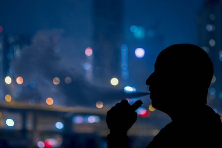 Man with electronic cigarette and smoke vapping with city bokrh lights backgroundの写真素材