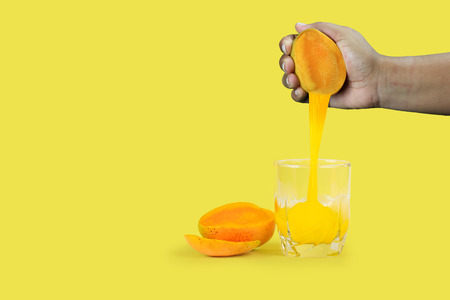 Hand squeezing mango juice into glassの写真素材