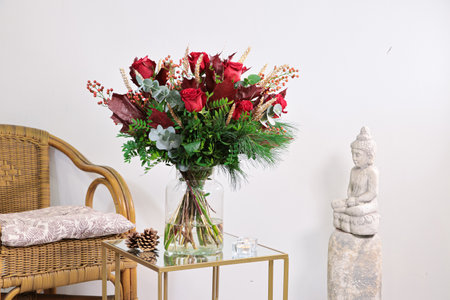 Bouquet of red flowers in vase on glass table and wicker chairの写真素材