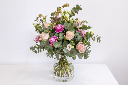 Bouquet of champagne roses, carnations and eucalyptus in a glass vase on a white background.の写真素材