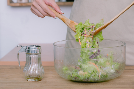 Young woman happy with preparing a good cooking casual lifestyle is mixing salad in kitchen at home. The concept is healthy food.の写真素材