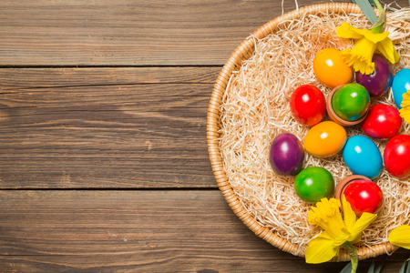Easter nest with colorful eggs and yellow daffodils on a wooden table.
