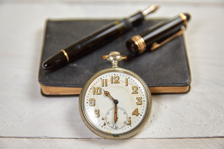 Antique fountain pen, old calendar and watch on a white wooden table
