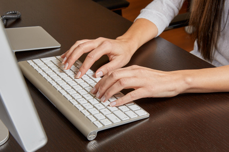 Woman typing on a computer keyboard on a wooden desk in front of a screen in the office.のeditorial素材
