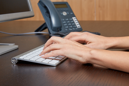 Woman typing on a computer keyboard on a wooden desk in front of a screen in the office.のeditorial素材