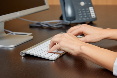 Woman typing on a computer keyboard on a wooden desk in front of a screen in the office.のeditorial素材