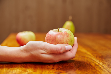 Woman holding an apple in the hand over a wooden tableの写真素材
