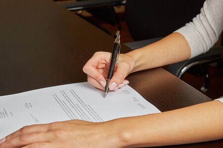 Woman writing on a white sheet of paper, signing a contractの写真素材