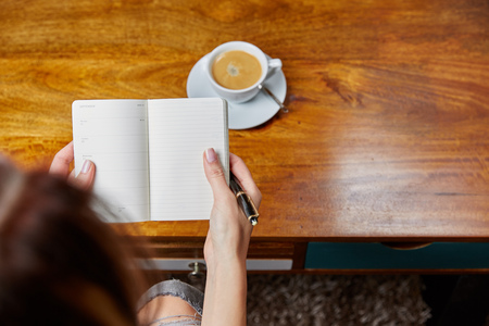 Woman writing in a book with coffee on a tableの写真素材
