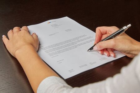 Woman writing on a white sheet of paper, signing a contractの写真素材