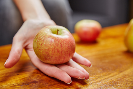 Woman holding an apple in the hand over a wooden tableの写真素材