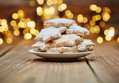 Cinnamon stars on a plate in front of christmas lightsの写真素材