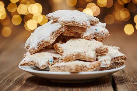 Cinnamon stars on a plate in front of christmas lightsの写真素材