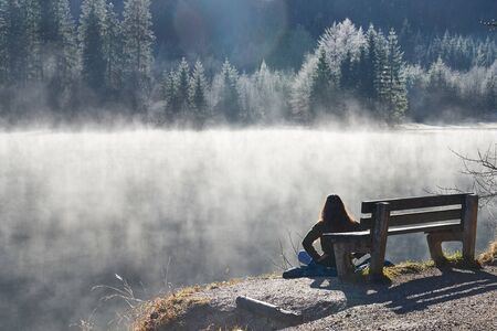 Mediating woman in front of a lake with fog and a forrestの写真素材