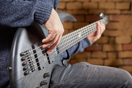 Bassist is playing a black bass in a club in front of a brick wallの写真素材