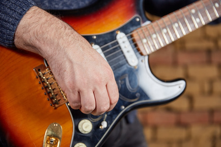 Hand of a guitar player turning the knobs of an electric guitar with bricks in the background