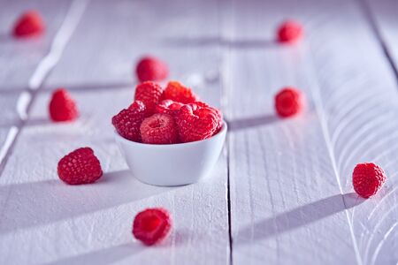 Light shines on raspberries on a white wooden tableの写真素材