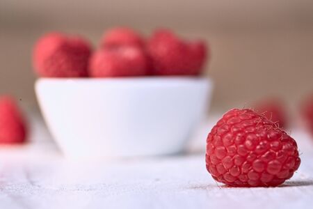 Single raspberry in front of  white bowl with ripe raspberriesの写真素材