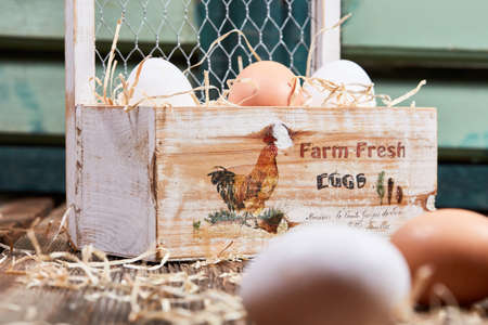 Fresh farm eggs with straw in a wooden box in front of a green windowの写真素材