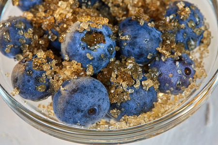 Blueberries and brown sugar in a glass bowl on a white tableの写真素材