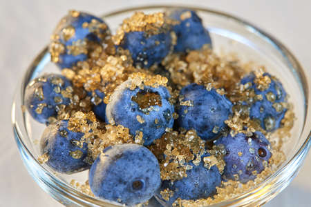 Blueberries and brown sugar in a glass bowl on a white tableの写真素材