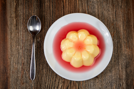 Yellow vanilla pudding with strawberry sauce on rown wooden tableの写真素材