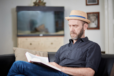 Man with beard and hat reads a book at home in an old buildingの写真素材