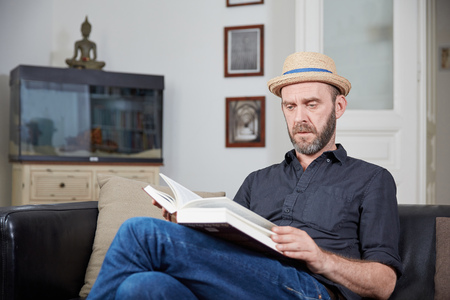 Man with hat reading a book in his leaving room in front of an aquariumの写真素材