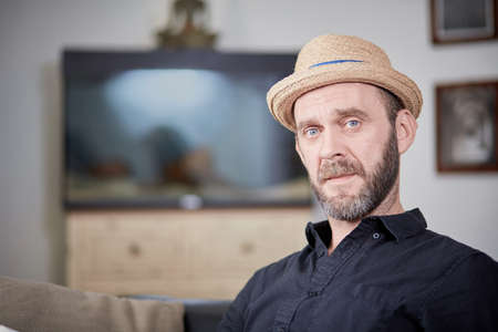 Cool guy with beard and hat looking to camera at home in front of aquariumの写真素材