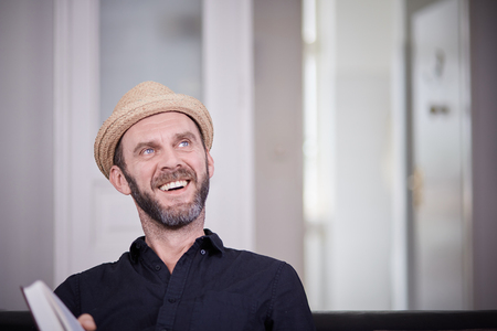 Hipster with beard and hat laughing at home in old building flatの写真素材