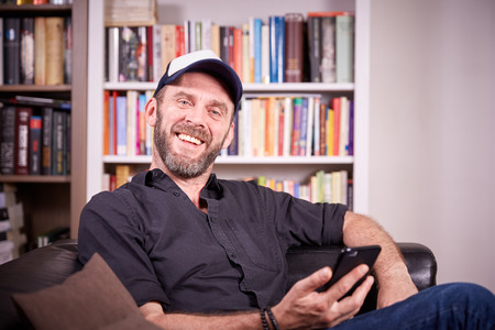 Man sitting on a couch in his living room with mobile phone laughing