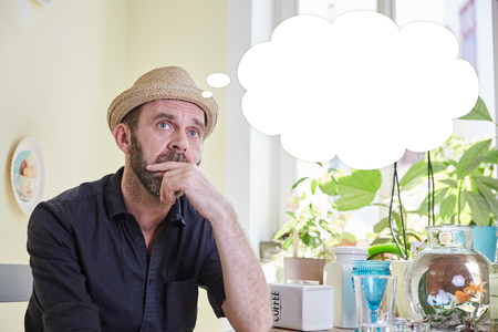 Man brooding with a thought bubble over his head sitting in a kitchen indoorsの写真素材