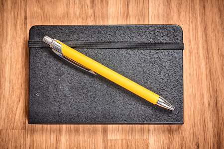 Closed notebook and yellow pen ballpoint on a brown wooden tableの写真素材
