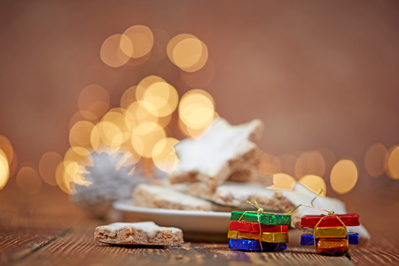 Christmas cinnamon stars on wooden  table with presents and background lightsの写真素材