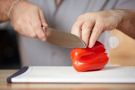 hand of a caucasian man cutting red pepper on a white boardの写真素材