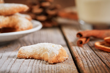 Single vanilla cookie vanilellekipferl on a wooden table with glass of milk and cinnamon rollsの写真素材
