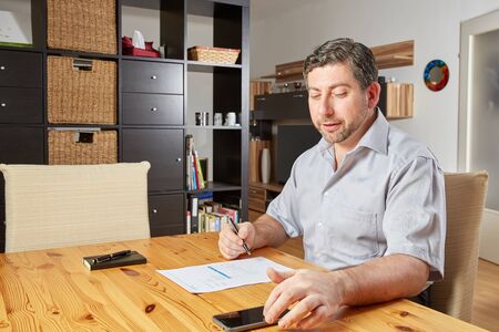 Caucasian man on wooden table at home with smartphone and documentの写真素材