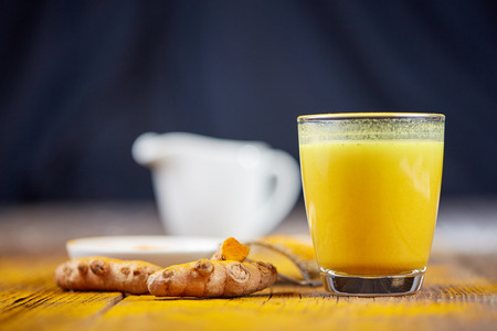 Turmeric tea golden milk with orange curcuma root on wooden tableの写真素材
