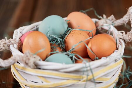 Easter basket with colored easter eggs and green grass on brown wooden tableの写真素材