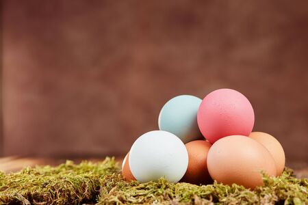 Pastel colored easter eggs on moss on a brown wooden table in front of brown backgroundの写真素材