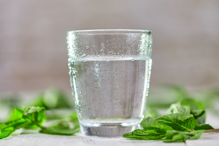 Glass of fresh cold water with green mint on white tableの写真素材