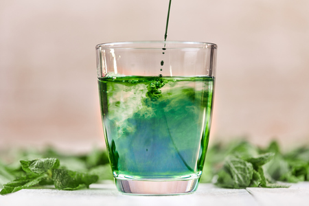 Green chlorophyll drink in glass with water on white table with green mintの写真素材