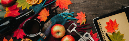 Autumn leaves, two cups of wine, red apples with plaid on old vintage wooden background. Top view with space for your text.の写真素材