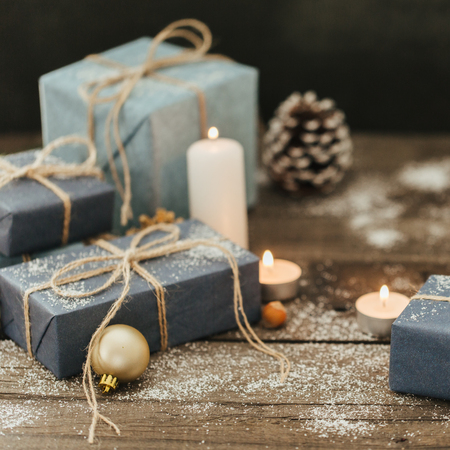 Festive Gifts with Boxes, Candle, Snow, Coniferous, Basket, Cinnamon, Pine Cones, Nuts on Wooden Background.の写真素材