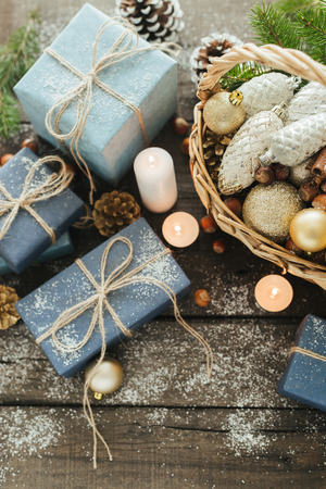 Festive Gifts with Boxes, Candle, Snow, Coniferous, Basket, Cinnamon, Pine Cones, Nuts on Wooden Background. With space for your text