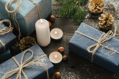 Festive Gifts with Boxes, Candle, Snow, Coniferous, Basket, Cinnamon, Pine Cones, Nuts on Wooden Background. With space for your textの写真素材